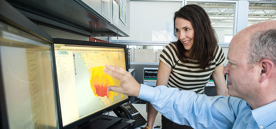 Photo of Suzanne Tegen of the Market and Policy Impact Analysis group at NREL's Strategic Energy Analysis Center and Nate Blair, Manager of the Energy Forecasting and Modeling group, looking at a computer screen showing a renewable energy risk performance model.